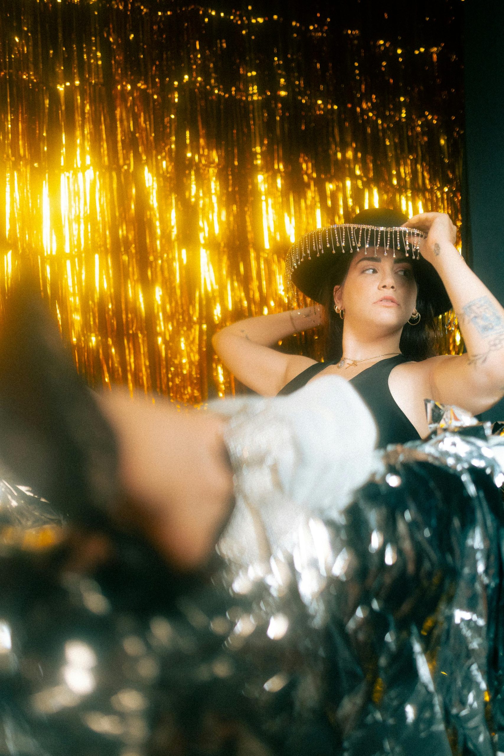 Woman posing in a festive setting with golden decorations and a fashionable hat.